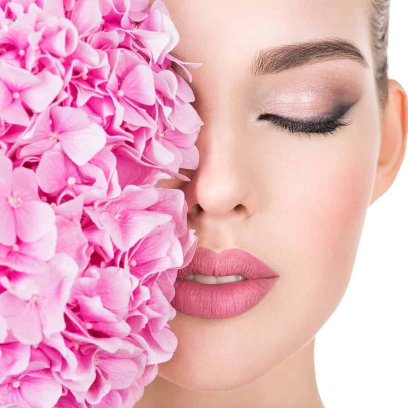 Young beautiful woman with flowers near face. Beauty treatment concept. Skin care. Pretty female with health, fresh skin of body. Lady with pink makeup of eyes.